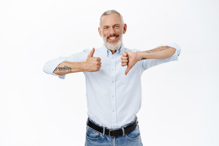 Handsome senior businessman showing thumbs up and thumbs down, like or dislike gesture, standing over white backgroundの写真素材