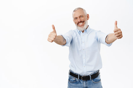 Smiling cheerful businessman, senior guy showing thumbs up in approval, like, standing against white backgroundの写真素材