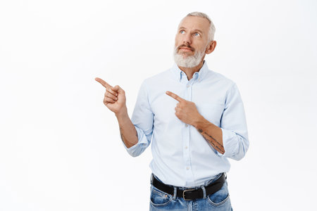 Senior business man pointing fingers left, showing advertisement, promo offer, standing over white backgroundの写真素材