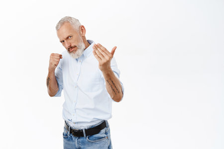 Image of serious senior man in shirt, clench fist and lure to come closer, fighting, standing over white backgroundの写真素材