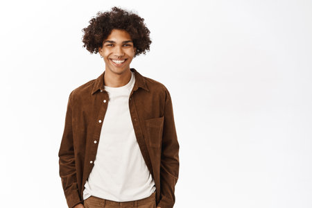 Portrait of smiling hispanic young man with curly hairstyle, looking casual, standing over white backgroundの写真素材
