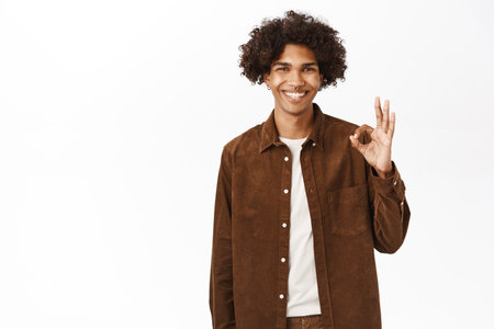Portrait of smiling hispanic guy shows okay, ok approval sign, agree with you, recommends course, stands over white backgroundの写真素材