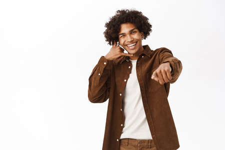 Call me. Happy young guy showing mobile phone gesture and pointing at you, asking your number, standing over white backgroundの写真素材