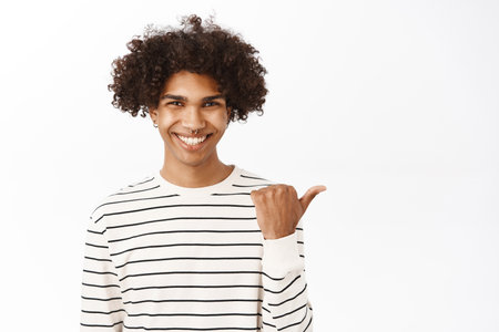 Close up portrait of young hispanic guy pointing finger right, showing advertisement, promo offer, announcement banner aside, standing over white backgroundの写真素材