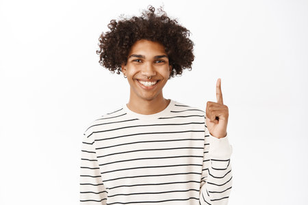 Happy smiling guy pointing finger up, showing advertisement on top, announcement or banner upwards, standing over white backgroundの写真素材