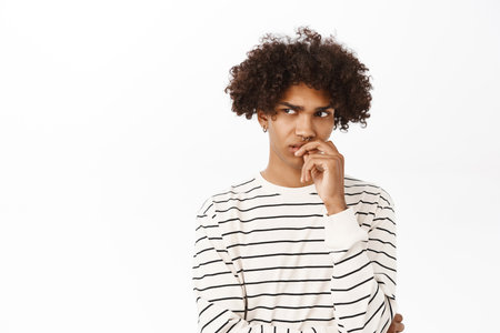 Close up portrait of hispanic guy with curly hair thinking, looking bothered by dilemma, pondering, standing over white backgroundの写真素材