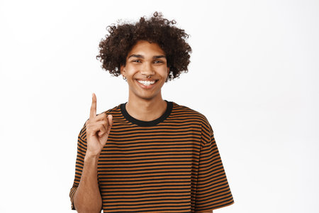 Portrait of young hispanic guy showing number one and smiling, pointing up, standing over white backgroundの写真素材