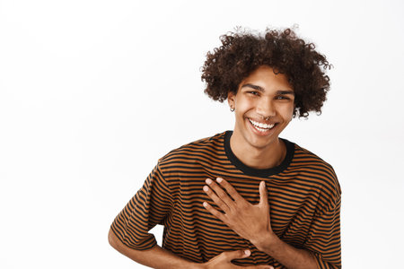 Portrait of handsome hispanic guy laughing and smiling, standing in casual tshirt over white backgroundの写真素材