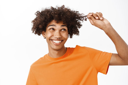 Close up portrait of young man touching his curls, boy with curly hair smiling and laughing, standing over white background in orange t-shirtの写真素材