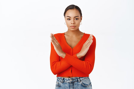 Stop. Upset african american woman, showing cross, disapprove gesture, prohibit action, standing in red blouse over white backgroundの写真素材