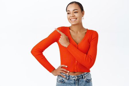 Portrait of happy smiling african american woman, 25 years old, pointing finger upper left corner, showing advertisement, standing over white backgroundの写真素材