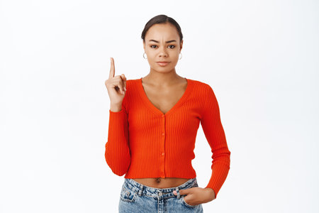 Portrait of smiling confident woman pointing finger up, showing announcement, shop promo, standing over white backgroundの写真素材