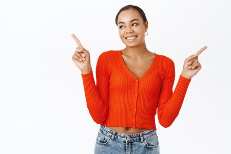 Portrait of smiling young healthy woman, pointing fingers sideways, left and right side, showing variants, standing over white backgroundの写真素材
