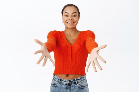 Portrait of excited young woman, reaching hands forward, stretching out arms for hug, taking, receiving something, standing over white backgroundの写真素材
