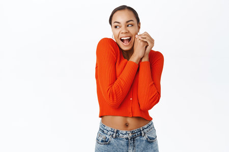 Cute young latina woman, looking aside with excitement, jumping from happiness, standing in red blouse over white backgroundの写真素材