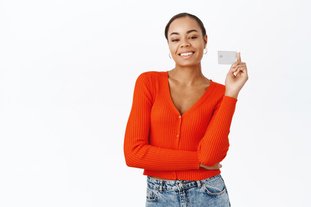Smiling young woman showing credit card, recommending bank services, posing in red blouse against white backgroundの写真素材