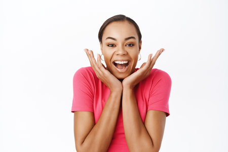 Close up of enthusiastic young woman, looking surprised and amazed, impressed reaction, standing over white backgroundの写真素材