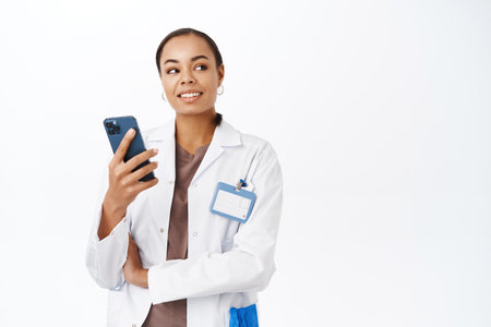 Online medical help. Young female doctor, therapist holding mobile phone, answer patients messages on healthcare app, standing over white backgroundの写真素材