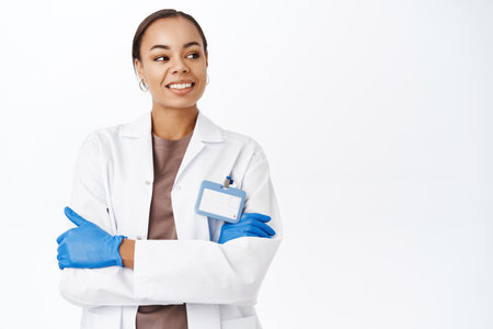 Smiling clinic doctor in medical gloves, looking aside with confident and happy face, standing over white backgroundの写真素材