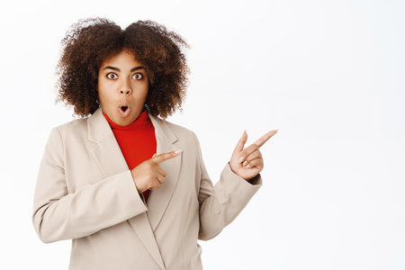 Surprised african american businesswoman, looks amazed, say wow and point right at direction, shows banner or company logo, advertising, standing over white backgroundの写真素材