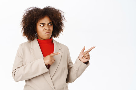 Angry african american business woman, pointing and looking right at empty space, disappointed in smth, standing over white backgroundの写真素材