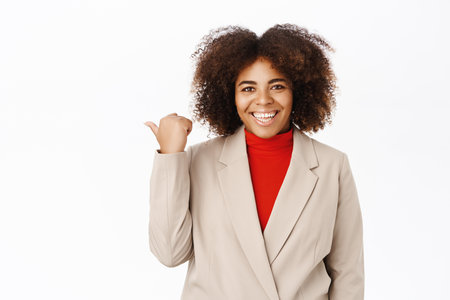 Look that way. Smiling african american businesswoman pointing left, showing advertisement, business logo, standing over white backgroundの写真素材