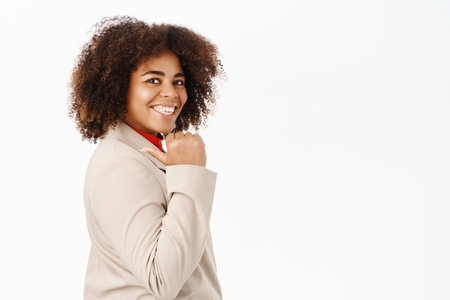 Smiling businesswoman points behind her shoulder at advertisement, standing in business suit over white backgroundの写真素材