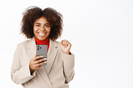 Excited businesswoman with mobile phone, stands over white backgroundの写真素材