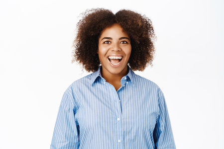 Excited african american young woman, looking amazed and fascinated, standing over white backgroundの写真素材