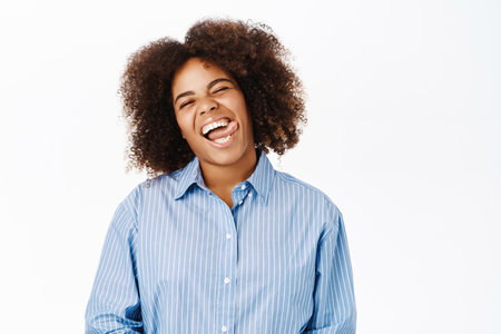Positive african american woman, shows her white healthy smile, sticking tongue, standing over white backgroundの写真素材