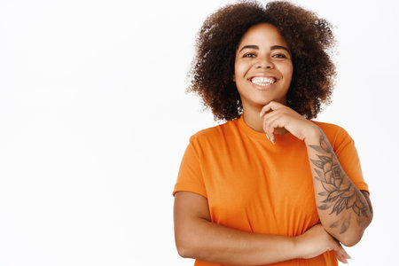 Portrait of modern smiling woman with tattoos, wears orange t-shirt, looks happy, stands over white backgroundの写真素材