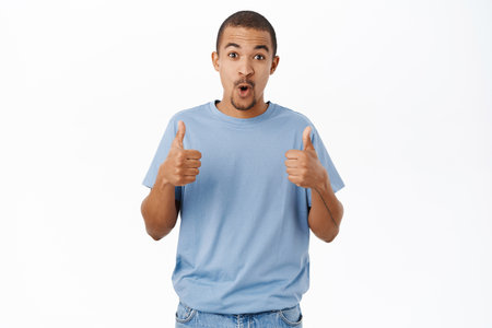 Smiling arab man shows thumbs up, recommends, gives positive feedback and his approval, stands over white backgroundの写真素材