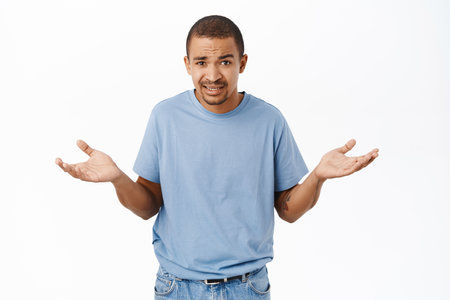Portrait of arab guy looks confused, shrugs with hands sideways, stands over white backgroundの写真素材