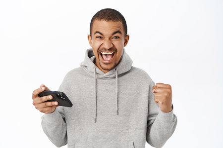 Excited man holding mobile phone and credit card, celebrating victory on smartphone, winning on telephone, standing over white backgroundの写真素材