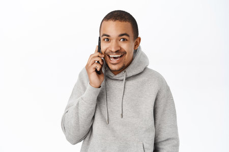 Portrait of happy young man talking on mobile phone, receive and call, speaking to someone on smartphone and smiling, standing over white backgroundの写真素材