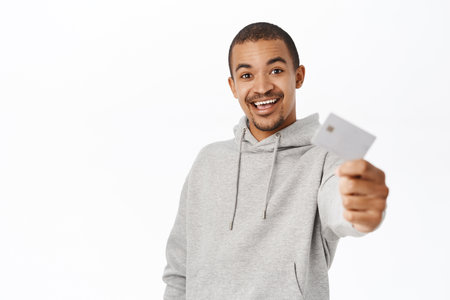 Portrait of happy young man receives his banking card, showing credit card and smiling, standing over white backgroundの写真素材