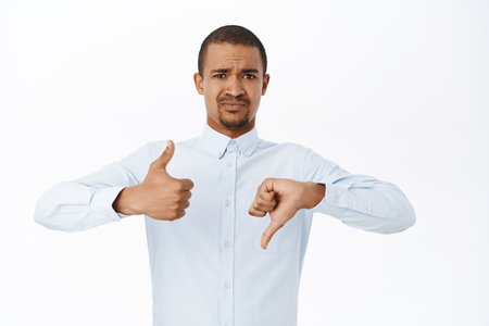 Like or dislike. Handsome man shows thumbs up and thumbs down, negative or positive feedback, stands over white backgroundの写真素材