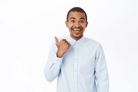 Smiling arab man pointing left, showing direction, company logo or banner aside, standing over white background in blue collar shirtの写真素材