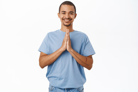 Smiling handsome guy holds hands in namaste, praying gesture, thank you sign, standing over white backgroundの写真素材