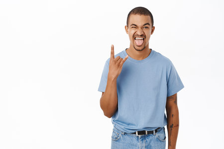 Enthusiastic guy shows rock on, heavy metal finger sign and looking joyful, having fun, standing over white backgroundの写真素材