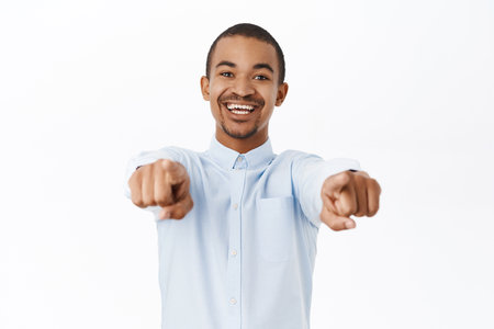 Young man pointing fingers at camera, inviting or congratulating you, praising, standing over white backgroundの写真素材