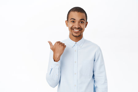 Smiling arab man pointing left, showing direction, company logo or banner aside, standing over white background in blue collar shirtの写真素材