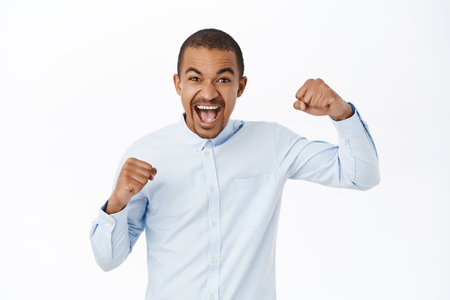 Celebrating success. Excited young man scream of joy, winning and triumphing, feeling like champion, achieve goal, standing over white backgroundの写真素材