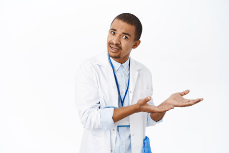 Portrait of male doctor pointing right, showing smth strange, looking confused, standing in white coat over white backgroundの写真素材