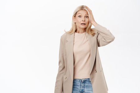Portrait of blond middle aged woman, mature lady looks confused, puzzled by smth, thinking, standing over white backgroundの写真素材