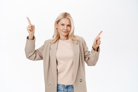 Portrait of beautiful middle aged woman pointing fingers left and right, showing direction, two variants, choices of products on sale, standing over white backgroundの写真素材