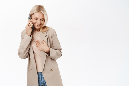 Portrait of stylish mature blond woman talking on mobile phone, having a call, using telephone cellular, standing over white backgroundの写真素材