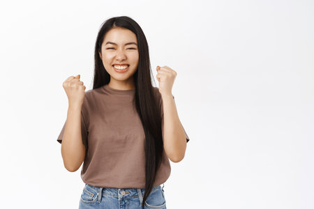 Yes, achievement. Happy asian girl wins, celebrates success and victory, triumphs, makes fist pumps, stands over white backgroundの写真素材