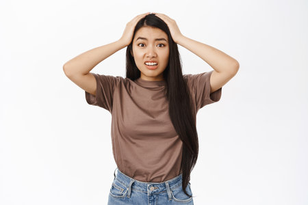 Oh my gosh. Shocked and worried asian woman, looking concerned and anxious, panicking, standing over white backgroundの写真素材
