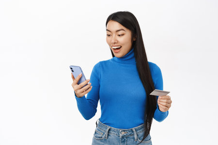 Online shopping. Happy asian woman using mobile phone and credit card, registrating bank account on smartphone app, order on website, white backgroundの写真素材